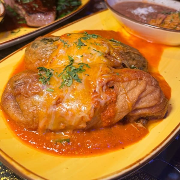 Two Chilangos Restaurant enchiladas covered in red sauce, melted cheese, and cilantro on a yellow plate.