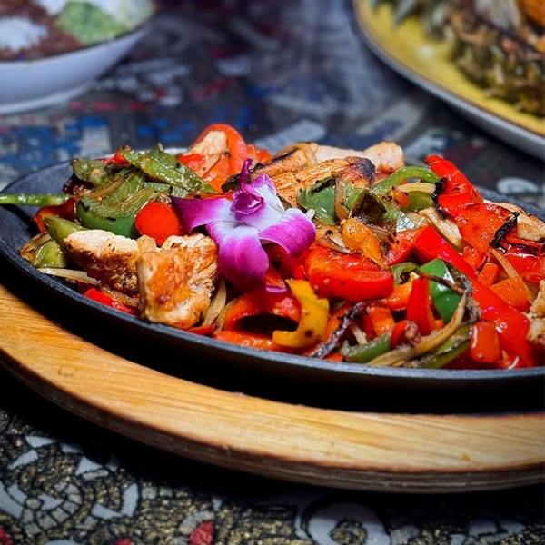 Sizzling chicken fajitas with colorful bell peppers and onions, garnished with a purple orchid.