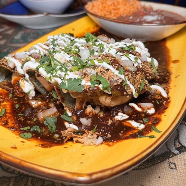 Chilangos Restaurant's enchiladas with rich mole sauce, crema, cilantro, and onions, served with rice and beans.