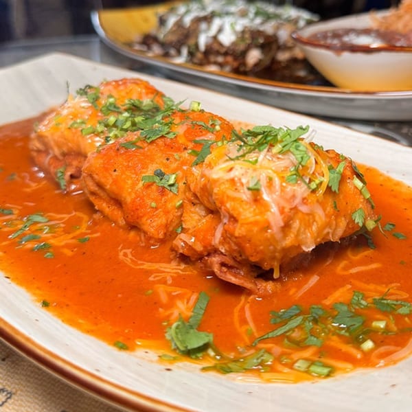 Three Chilangos Restaurant enchiladas covered in red sauce, cheese, and cilantro on a white plate.