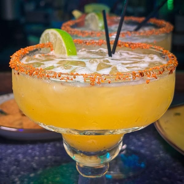 Two Chilangos Restaurant margaritas with chili-lime rims, lime wedges, and black straws on a dark table.
